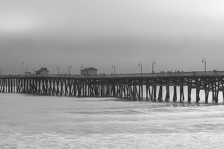 Black and white long pier extending over calm ocean water