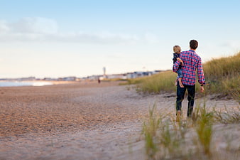 Father carrying son walking on sandy beach at sunset
