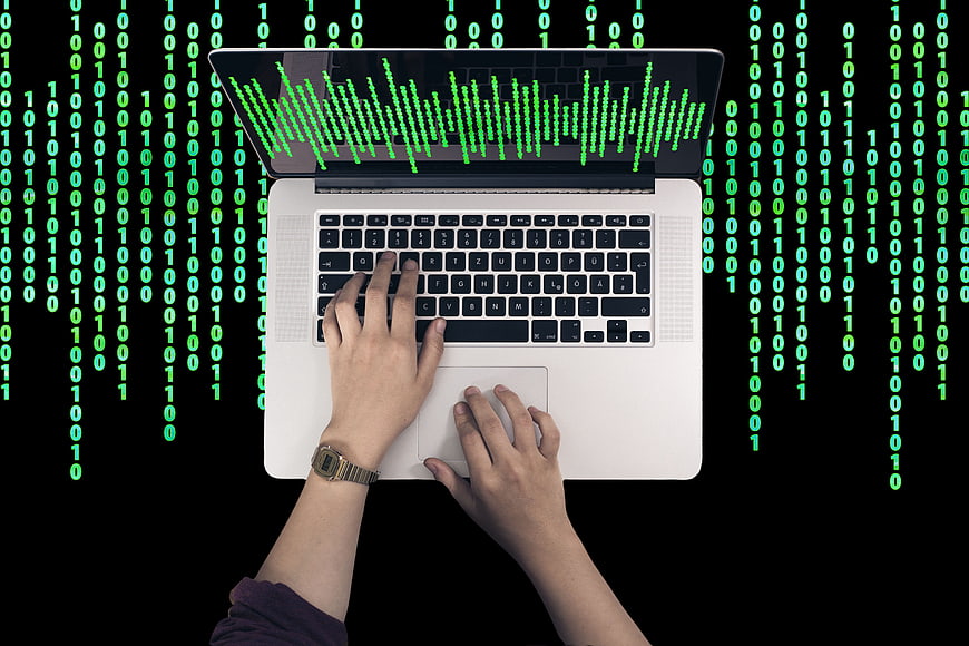Hands typing on laptop with green binary code background