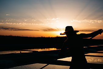 Silhouette of Man in Hat Rowing Boat at Sunset
