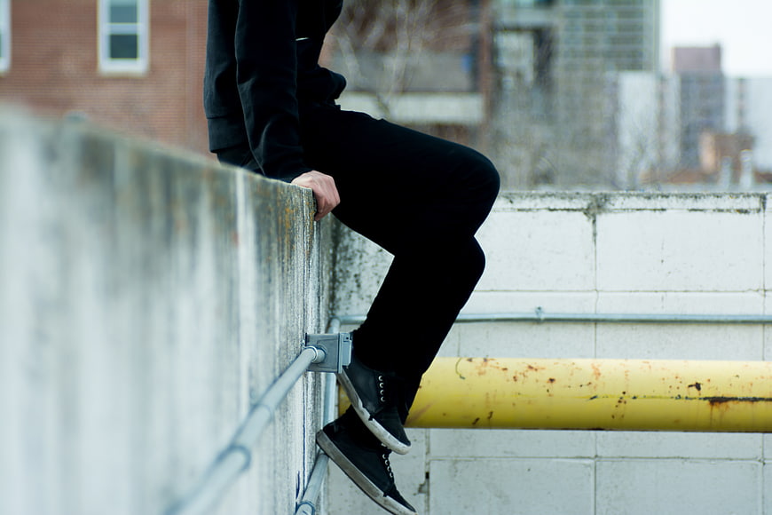 Person sitting on urban rooftop ledge with city background