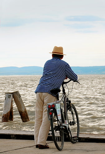 Man with bicycle looking out at lake from pier