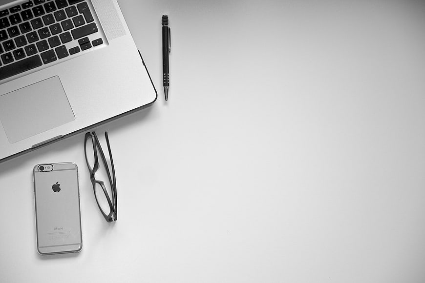 Minimalist workspace with laptop, smartphone, and glasses on white desk