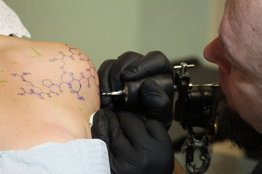 Tattoo artist inking complex chemical structure on client's shoulder