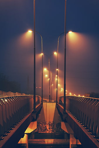 Foggy urban bridge with glowing streetlights at night