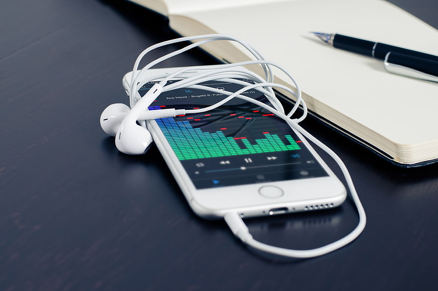 Smartphone with headphones and notebook on dark desk