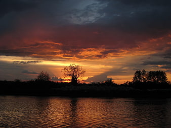 Dramatic sunset over river with silhouetted trees and clouds