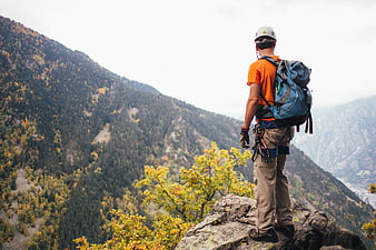Mountaineer with Backpack Standing on Rocky Mountain Peak Overlooking Forest