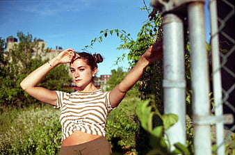 Young woman posing by chain-link fence in sunny field