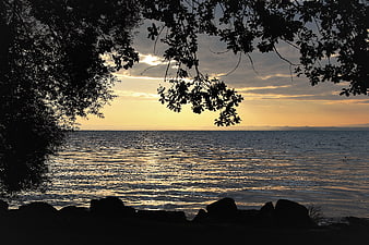 Serene Lake Sunrise Silhouette Framed by Dark Foliage and Rocks