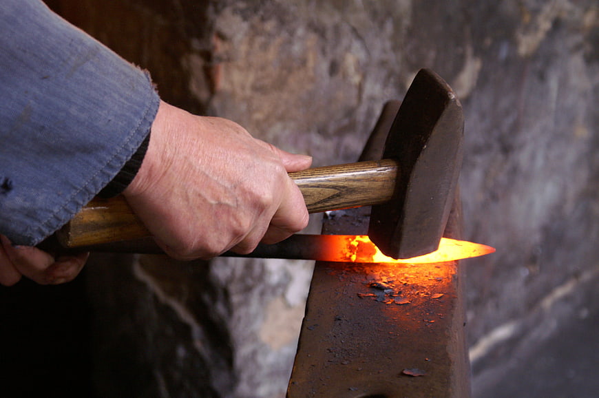 Blacksmith hammering glowing hot iron on anvil