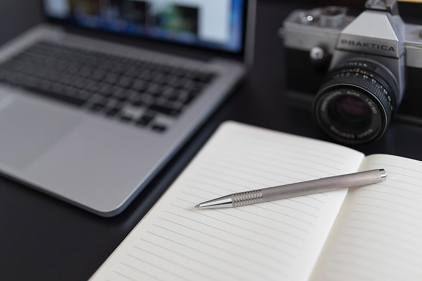 Silver mechanical pencil on notebook with laptop and vintage camera