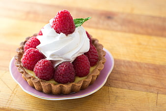 Raspberry tart with whipped cream on wooden table