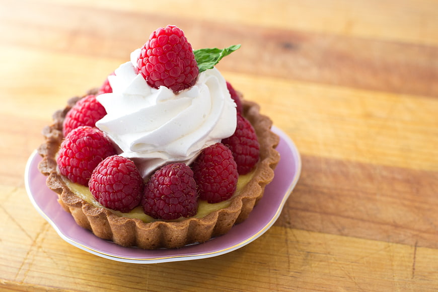 Raspberry tart with whipped cream on wooden table