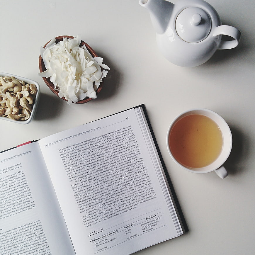 Flat lay of open book, tea, and healthy snacks on white table