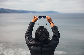 Woman in Leather Jacket Holding Sunglasses by the Sea