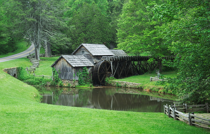 Historic wooden grist mill with water wheel in lush green valley