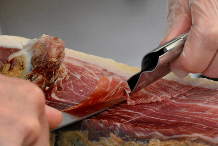 Close-up of hand slicing thin Iberian ham with knife