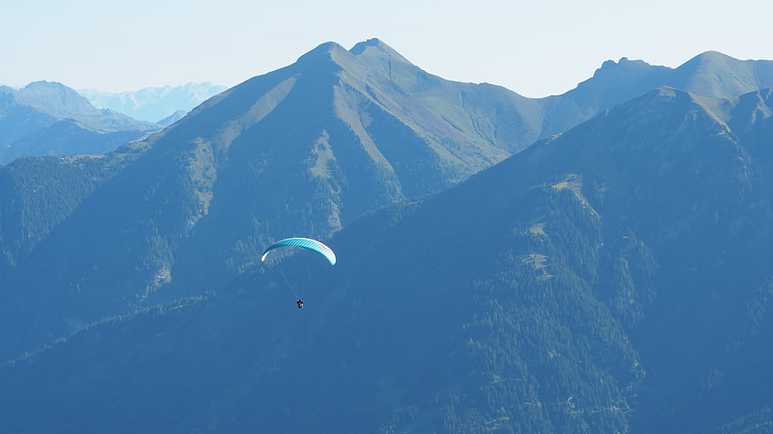 Paraglider soaring over majestic blue mountain peaks