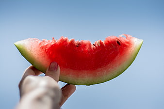 Hand Holding Fresh Watermelon Slice Against Blue Sky