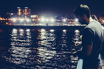 Man Fishing at Night with City Lights in Background