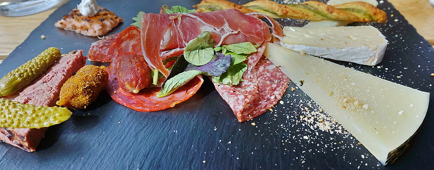 Gourmet charcuterie board with cured meats, cheese, and pickles on slate