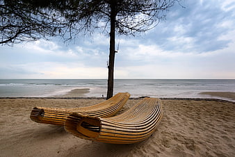 Modern curved wooden sun loungers on sandy beach