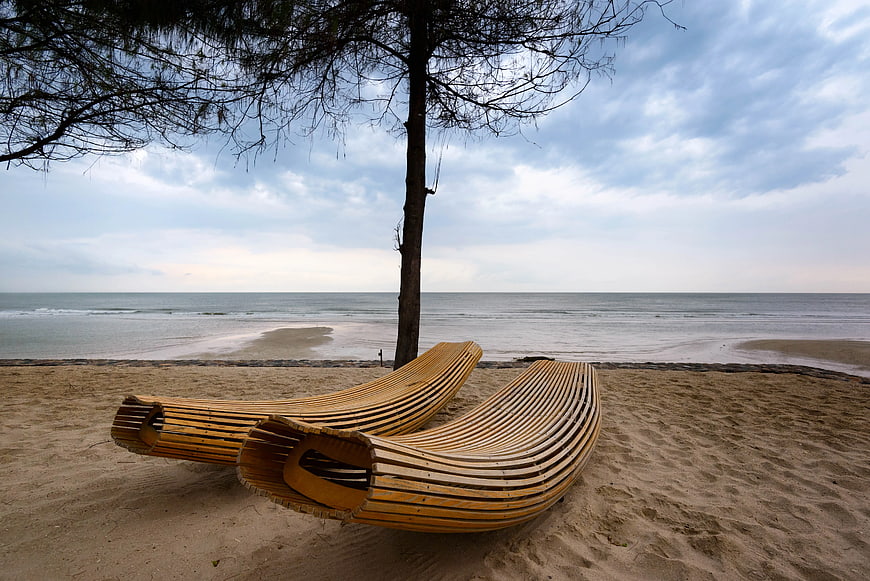 Modern curved wooden sun loungers on sandy beach