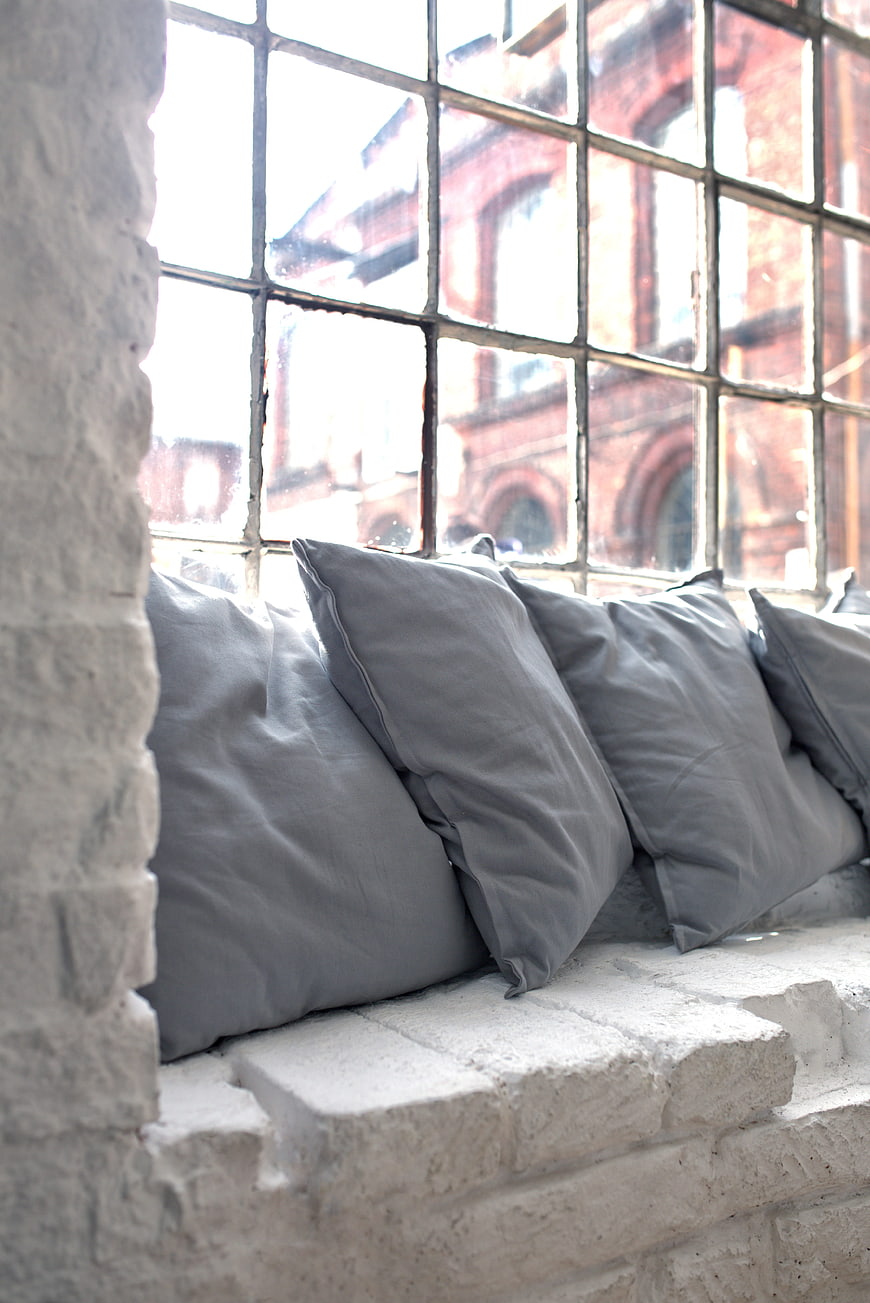 Gray pillows on a rustic brick windowsill with industrial window view