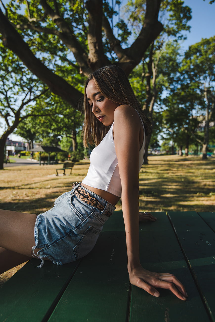 Young woman in white top and denim shorts sitting on park bench