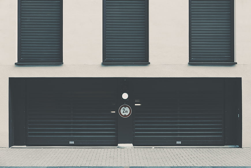 Minimalist modern building facade with black garage door and shutters