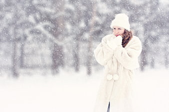 Woman in white fur coat and hat standing in heavy snow