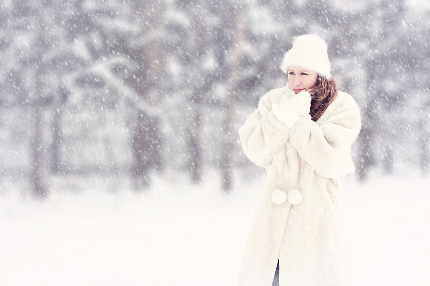 Woman in white fur coat and hat standing in heavy snow