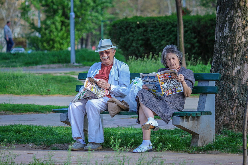Senior couple reading newspapers on a park bench
