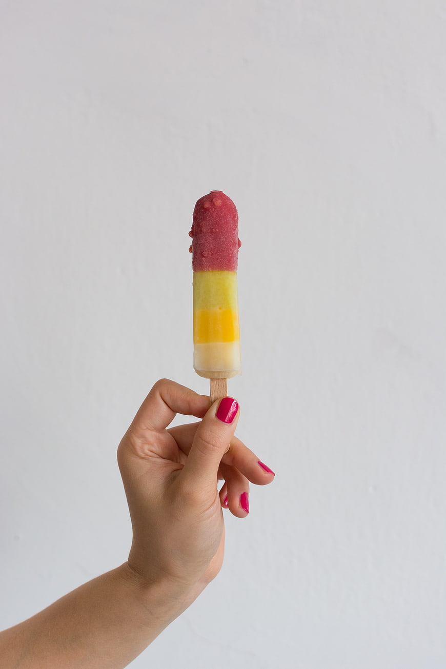 Hand holding colorful layered popsicle on white background