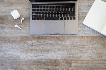 Top View of Laptop, AirPods, and Notebook on Wooden Desk