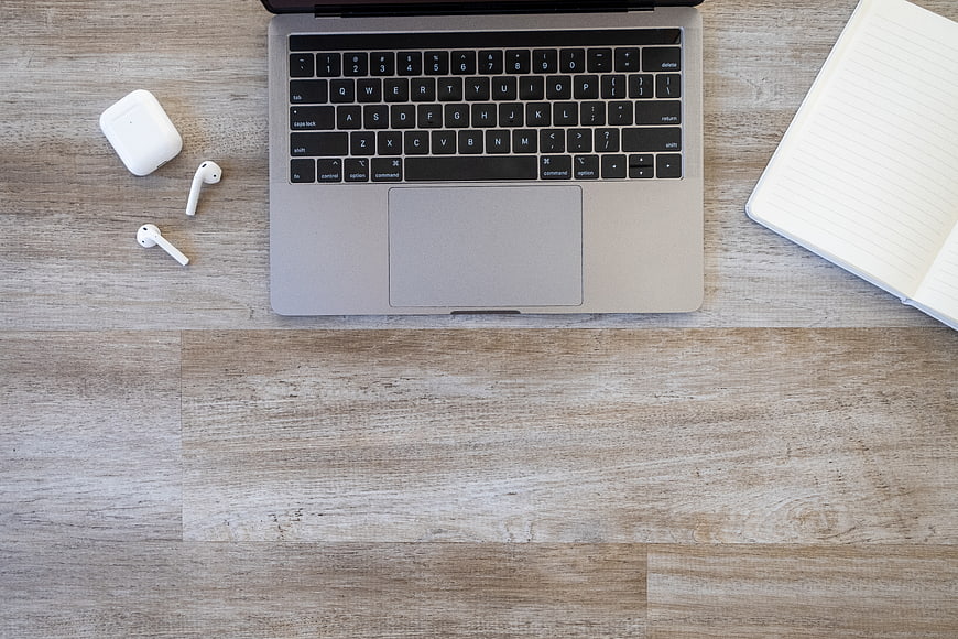 Top View of Laptop, AirPods, and Notebook on Wooden Desk
