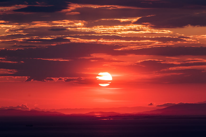 Dramatic Red Sunset Over Ocean and Mountains