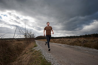 Man jogging on rural road under dramatic cloudy sky
