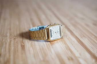 Gold rectangular wristwatch on wooden surface