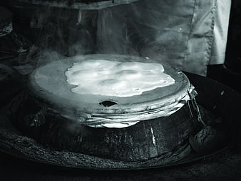 Black and white photo of steaming Thai rice cooking on clay stove