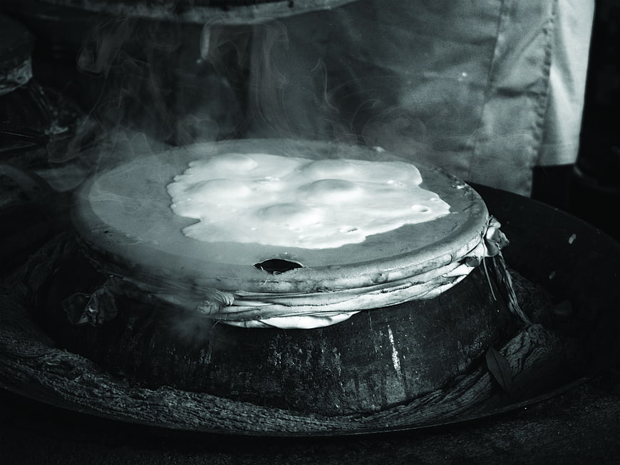 Black and white photo of steaming Thai rice cooking on clay stove