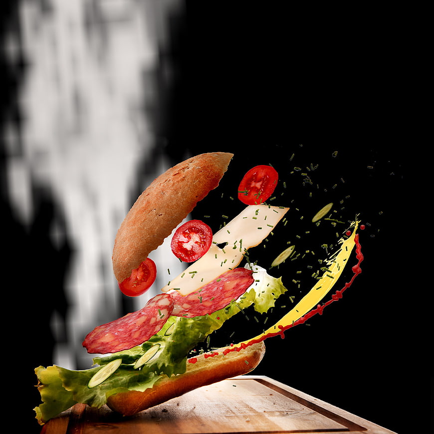 Exploding sandwich ingredients in mid-air on wooden board