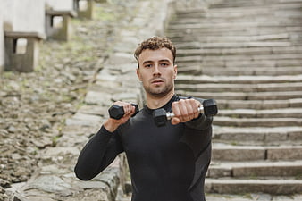 Fit Man Lifting Dumbbells Outdoors on Stone Stairs
