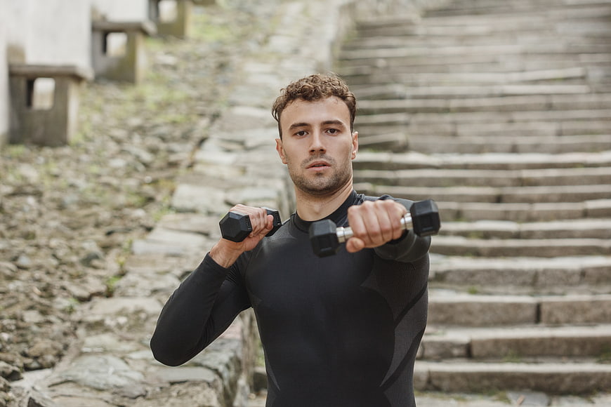Fit Man Lifting Dumbbells Outdoors on Stone Stairs