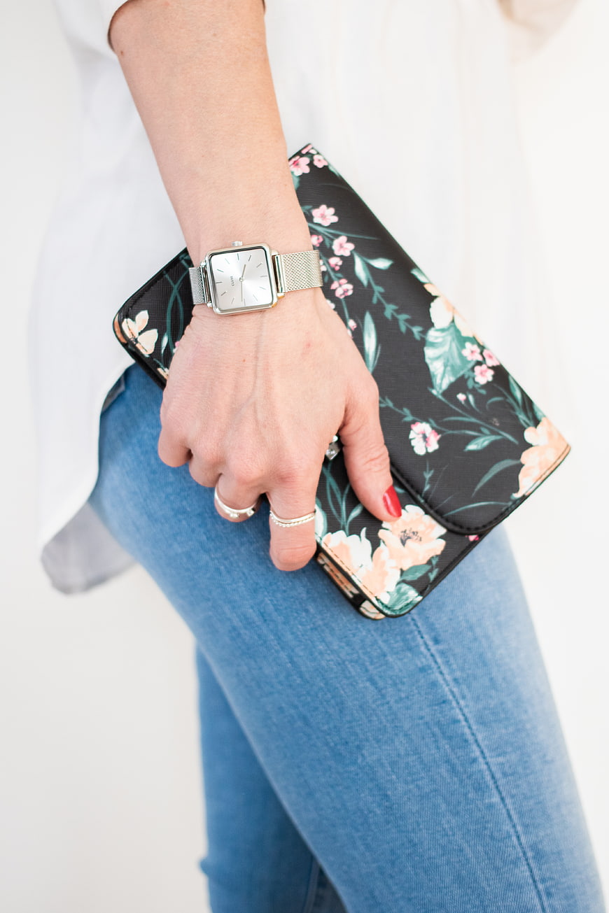 Woman holding floral clutch purse with silver watch