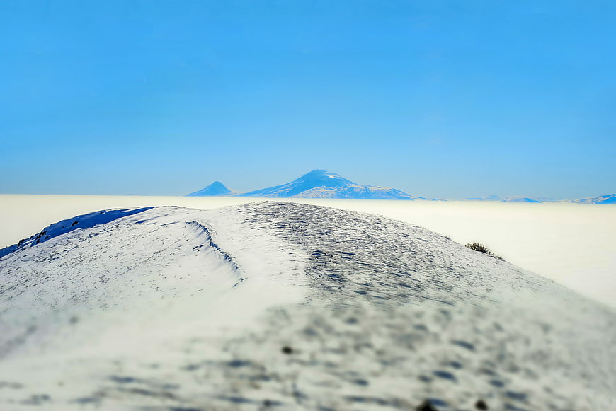 Snowy mountain ridge above sea of clouds with distant peaks