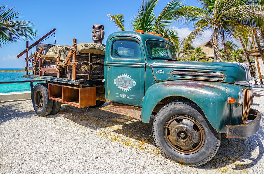 Vintage teal Ford truck parked on gravel near tropical beach