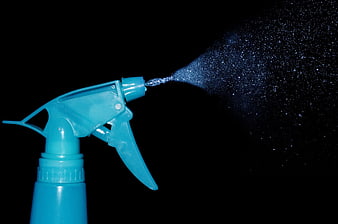 Blue spray bottle nozzle spraying water mist on black background