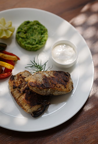 Grilled chicken breast with green pesto and sauce on white plate